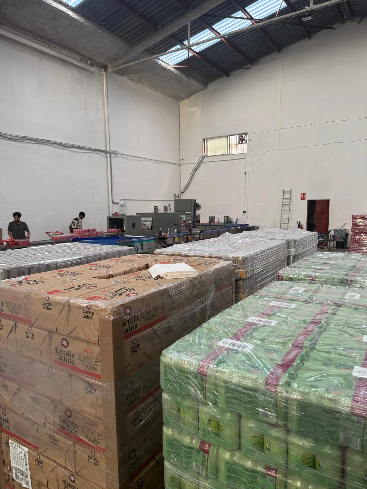 Interior de la nave de Catarroja: palés de bebidas listos para distribuir y línea de etiquetado y empaquetado al fondo